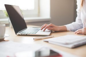 办公室内工作人员整理登录入口核实记录表格的场景，桌面摆放着笔记本电脑与文件夹